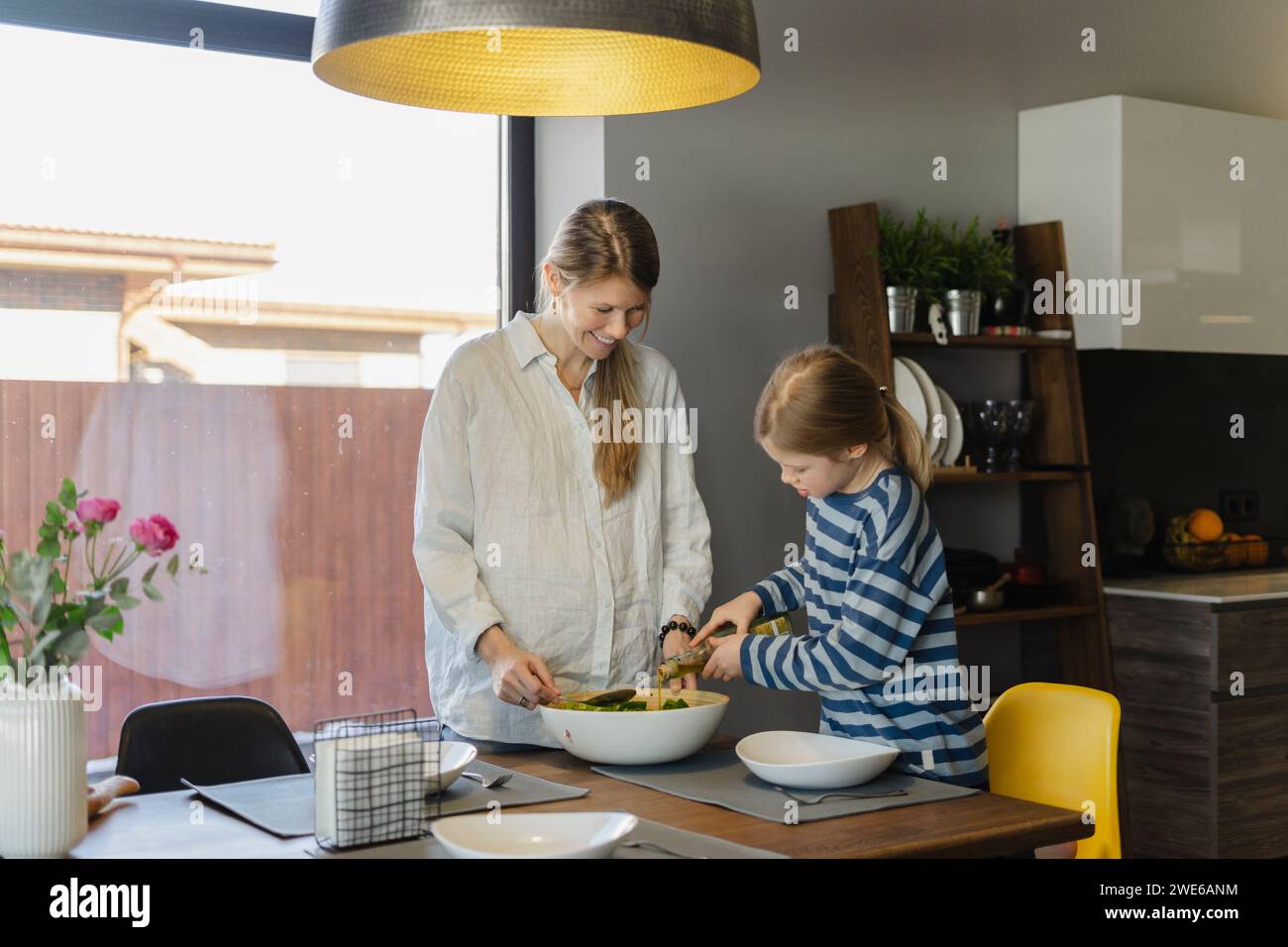 Smiling mother and daughter preparing food at dining table Stock Photo