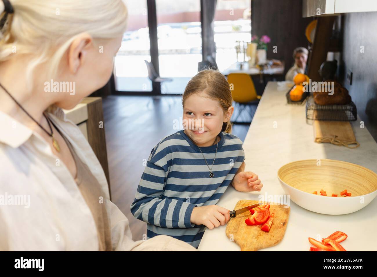Happy girl cutting red bell pepper with grandmother in kitchen at home Stock Photo