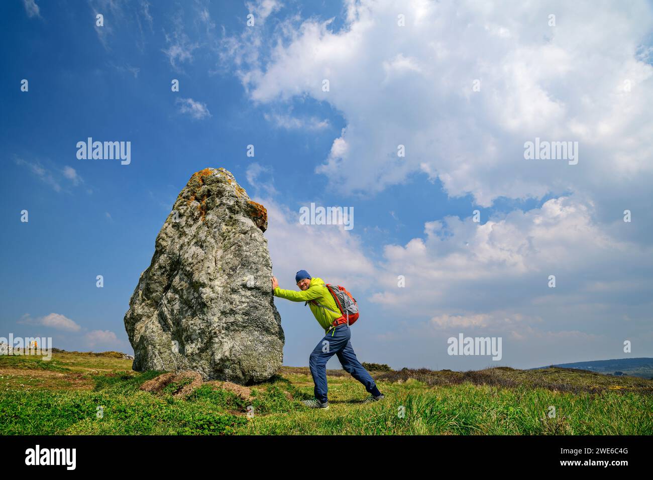 France, Brittany, Hiker pretending to push large menhir along Sentier Cotier route Stock Photo