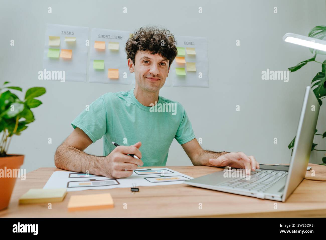 Web designer sitting with laptop and printout at desk in office Stock Photo