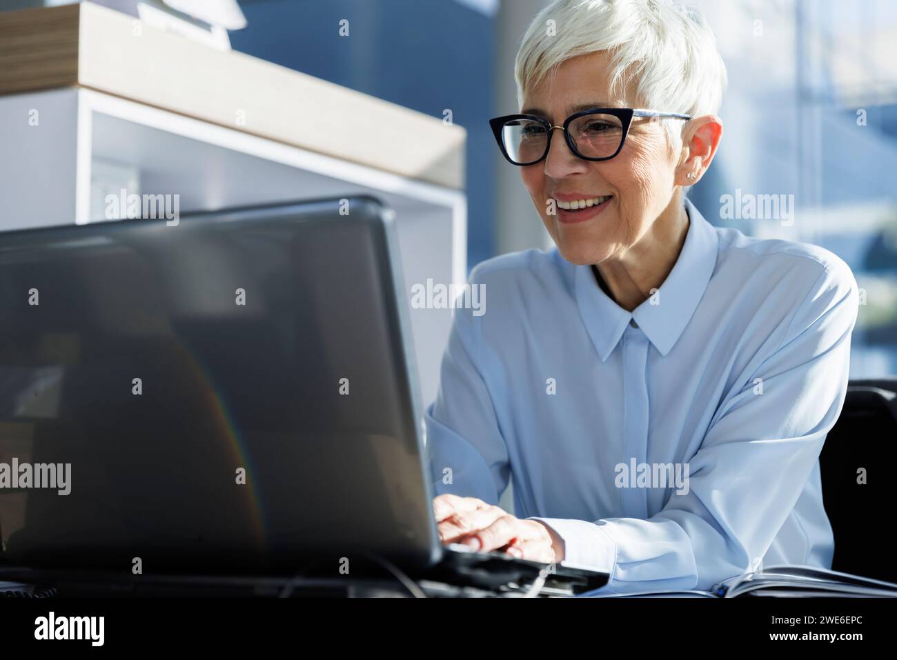 Happy businesswoman wearing eyeglasses and using laptop at office Stock Photo
