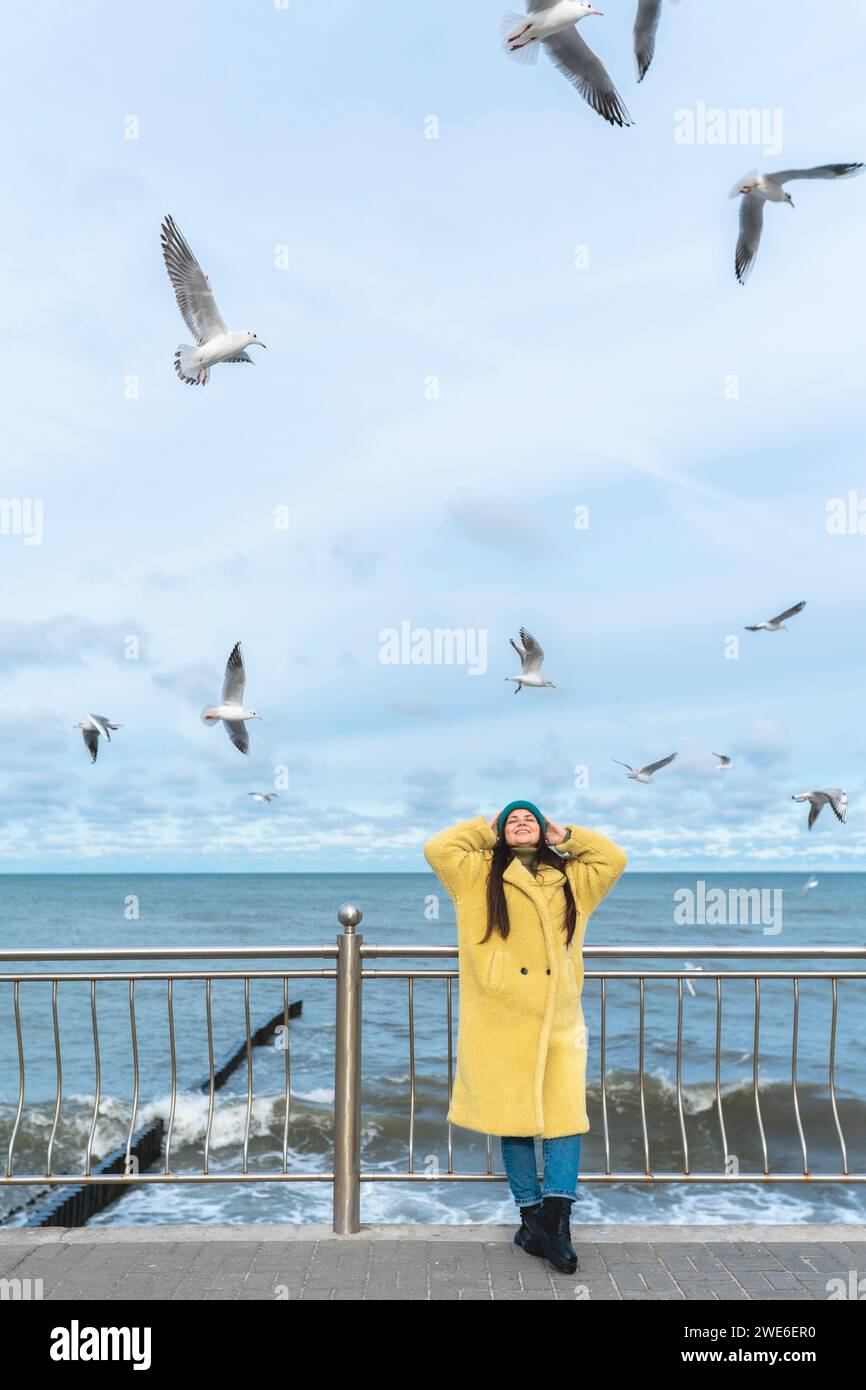 Carefree woman having fun near sea with seagulls flying in mid-air Stock Photo