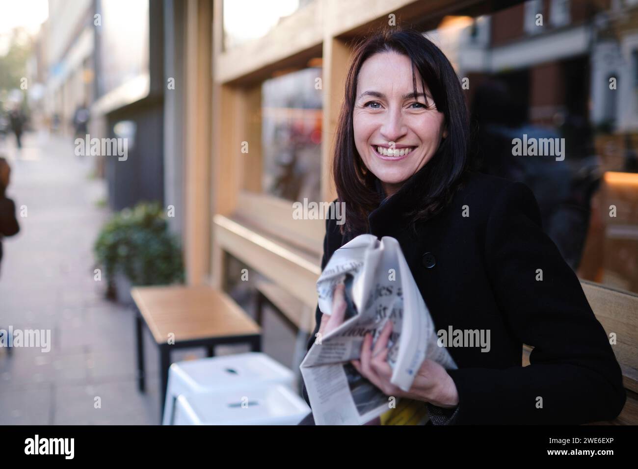 Smiling mature woman sitting with newspaper near building Stock Photo