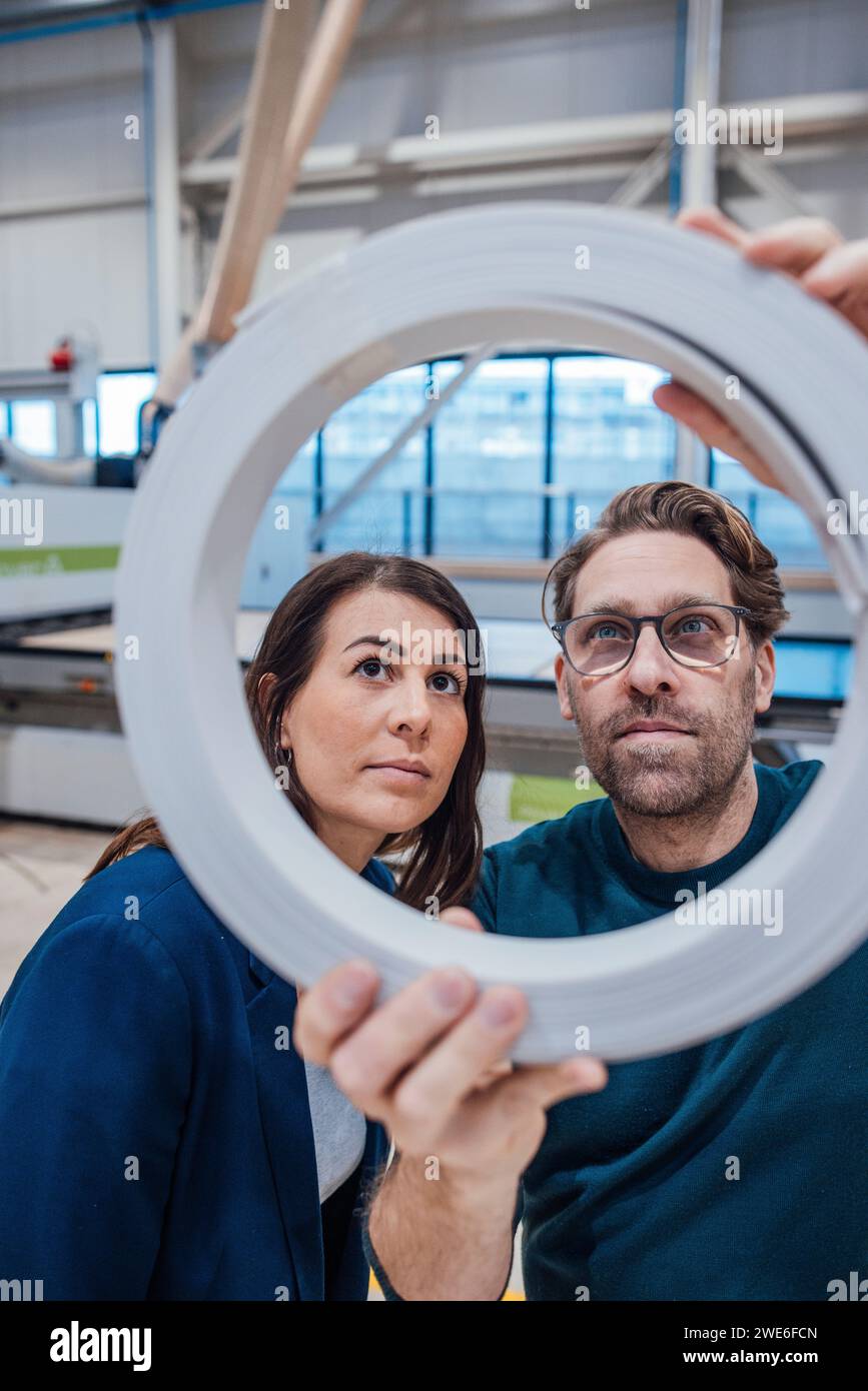 Colleagues analyzing circle shape machine part in workshop Stock Photo