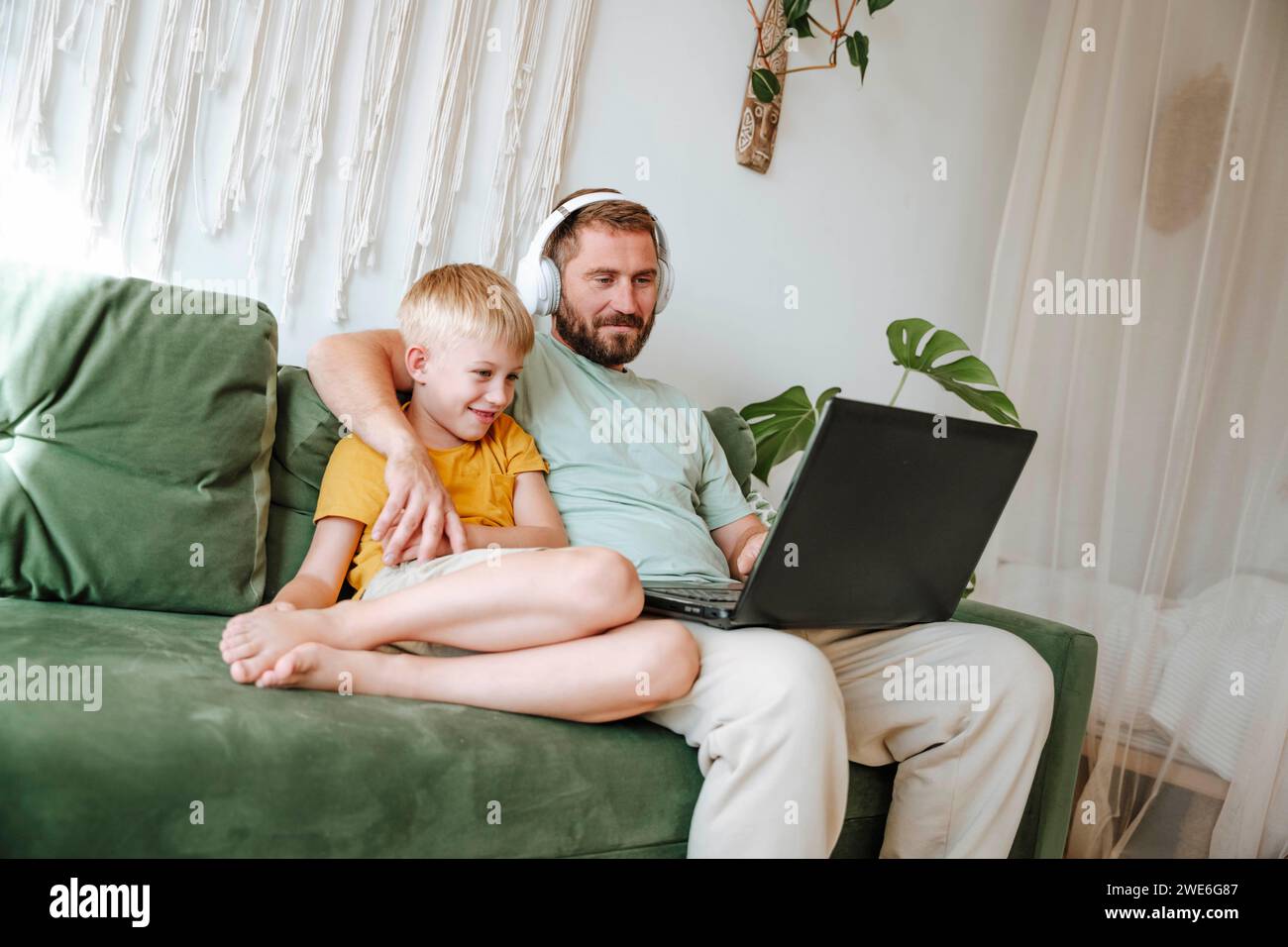 Father and son looking at a laptop while sitting on the couch at home Stock Photo