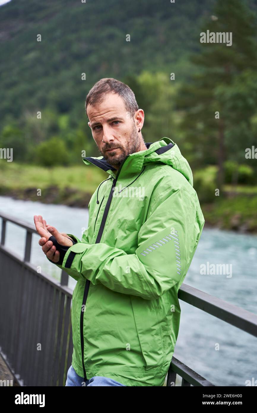 Man wearing green jacket and leaning on railing near river Stock Photo ...
