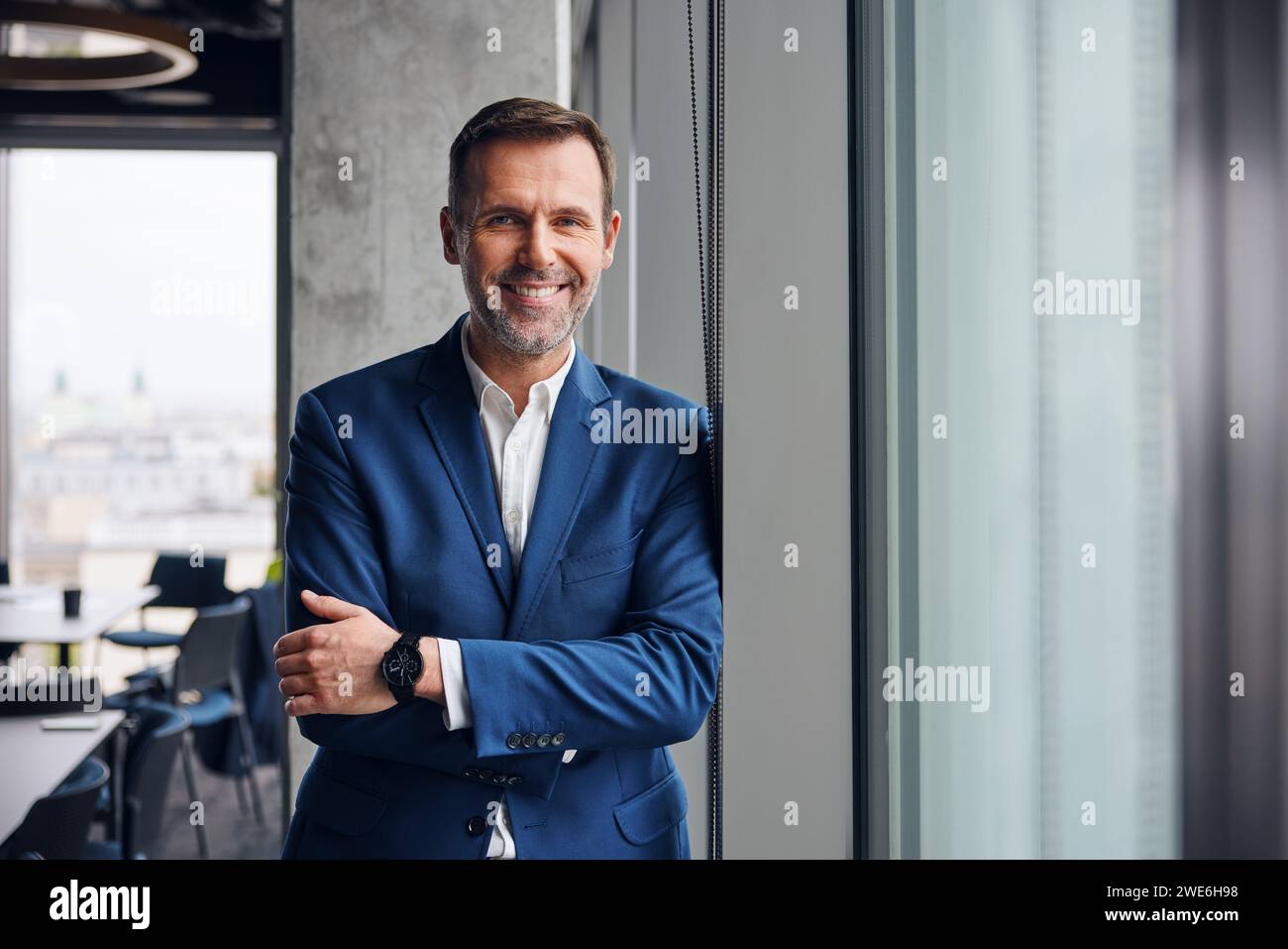 Happy businessman standing with arms crossed near window in office ...