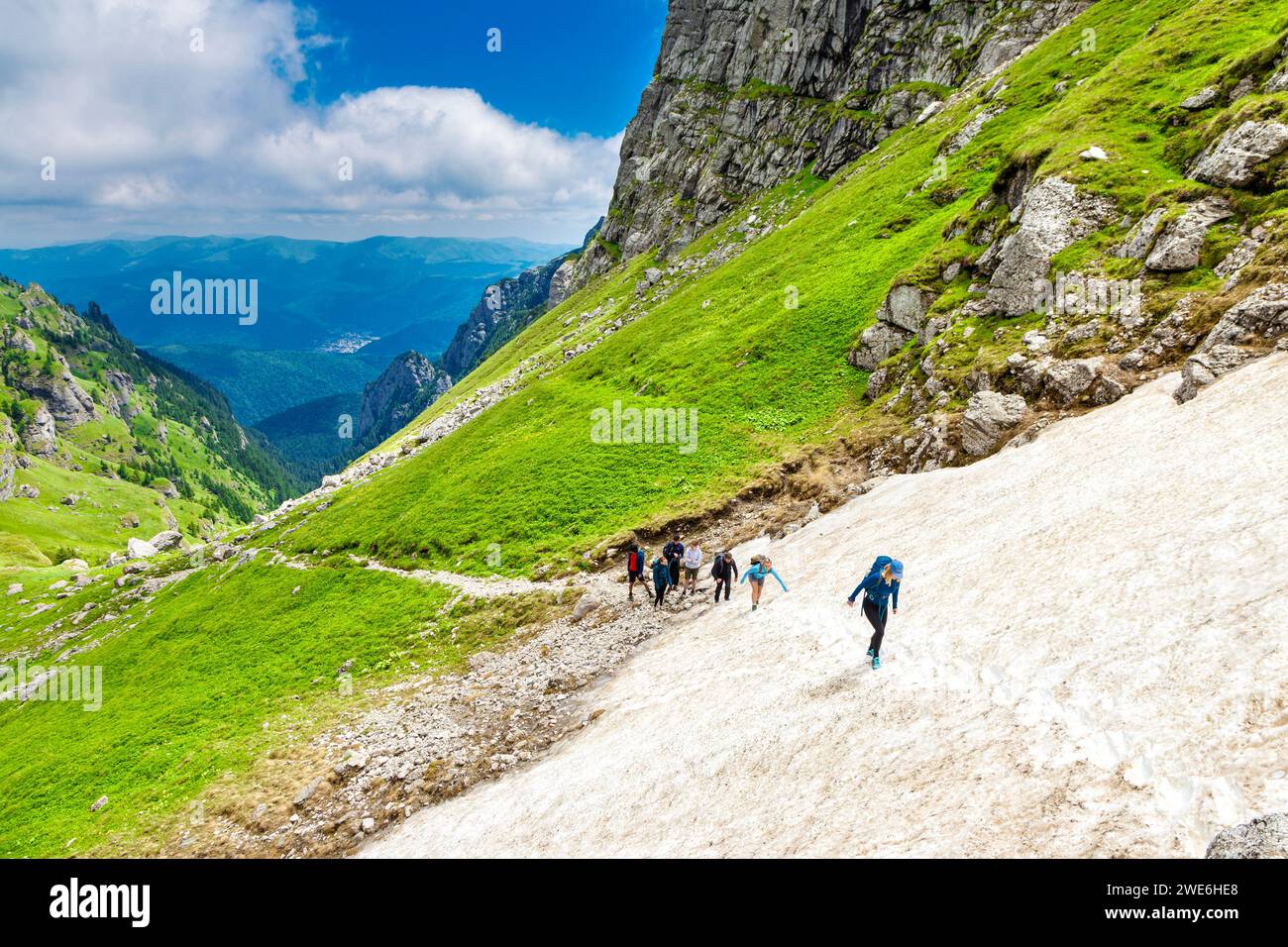 Group of hikers walking through snow on the trail from Busteni to the Omu Peak through Râul Valea Priponului valley, Bucegi Mountains, Romania Stock Photo