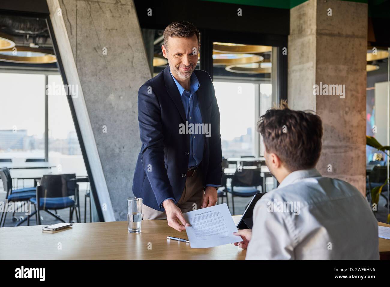 Smiling recruiter giving employment contract to candidate at desk Stock Photo