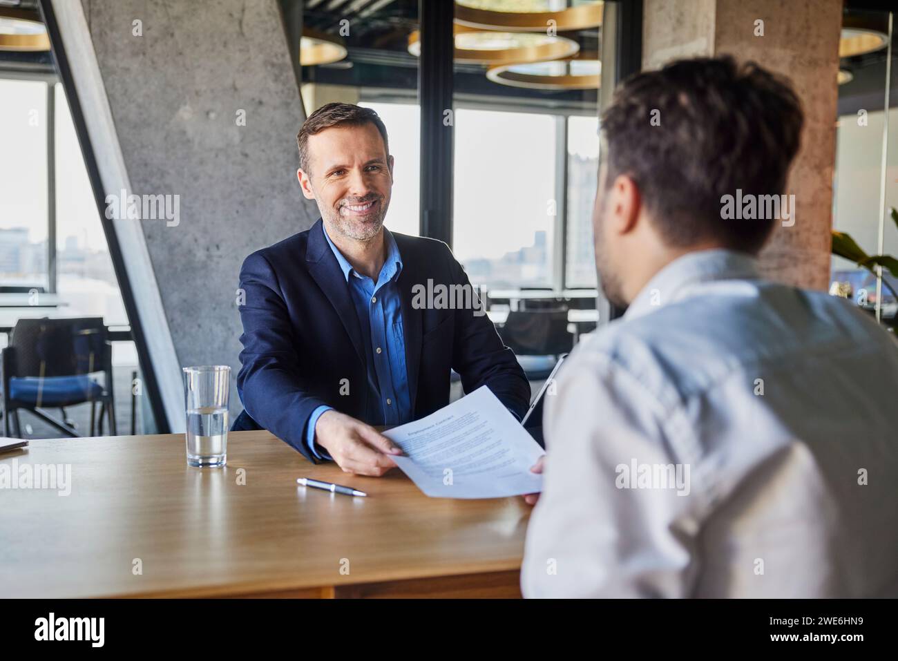 Happy recruiter giving employment contract to candidate at desk Stock Photo