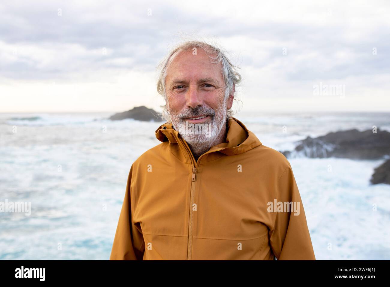 Smiling senior man wearing jacket and standing near sea Stock Photo