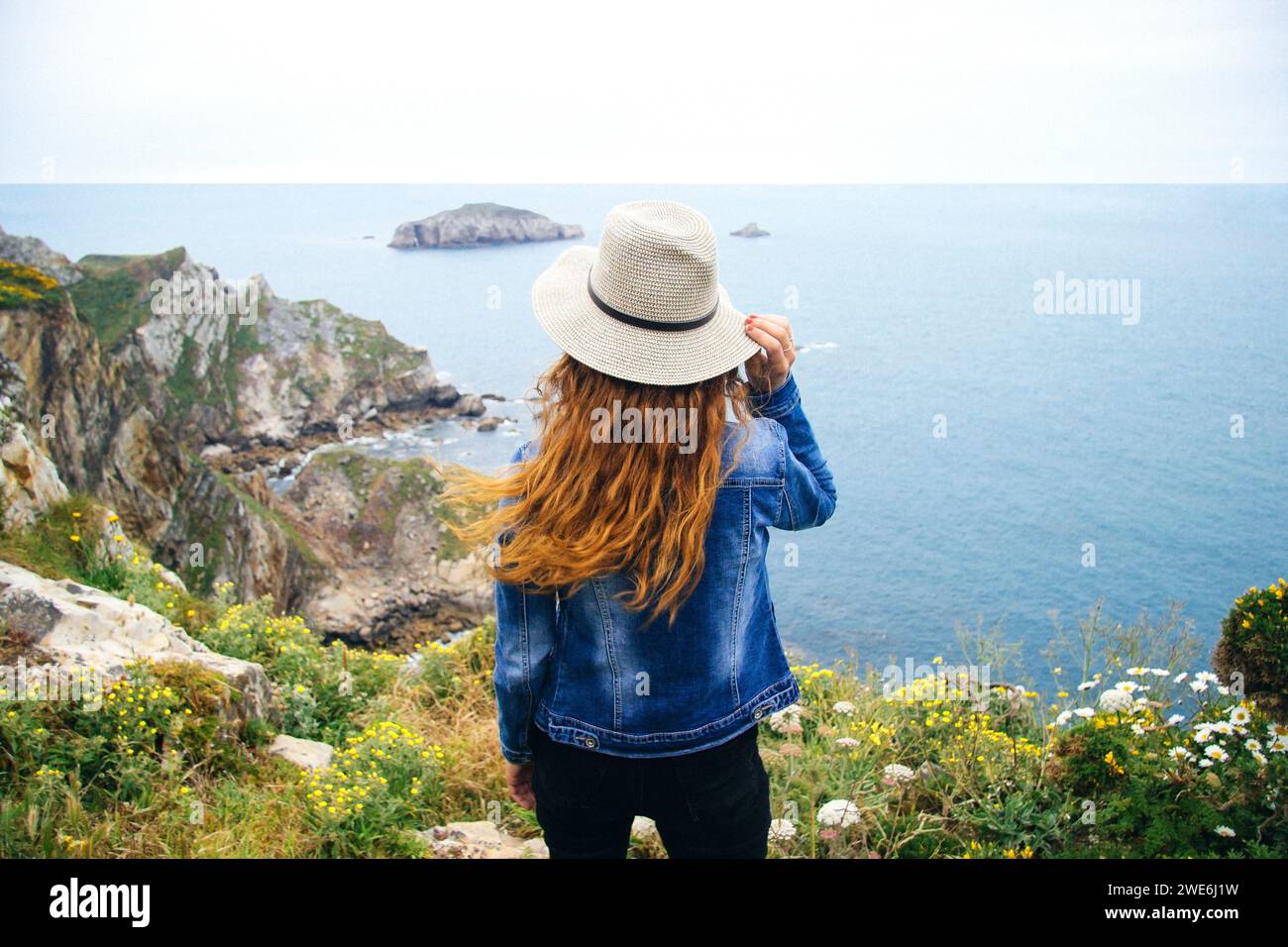 Redhead woman standing on cliff and looking at sea in Asturias, Spain Stock Photo