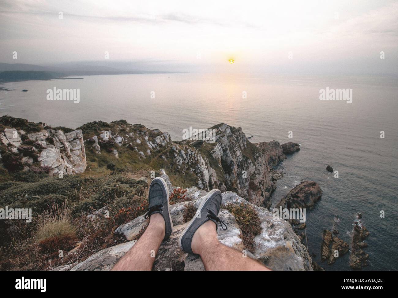 Young man sitting on cliff near sea at sunset Stock Photo