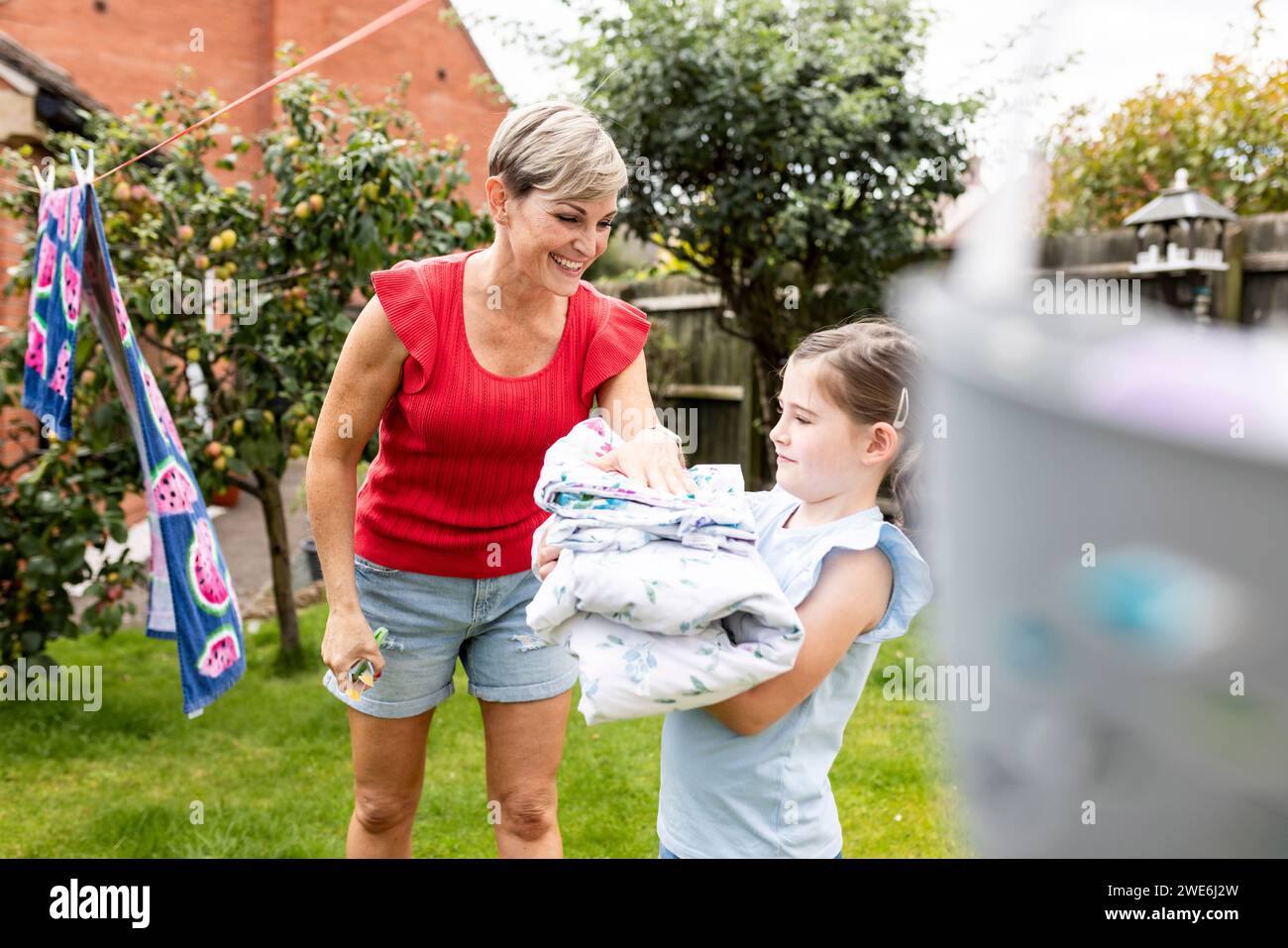 Daughter helping mother removing clothes from clothesline in back yard Stock Photo
