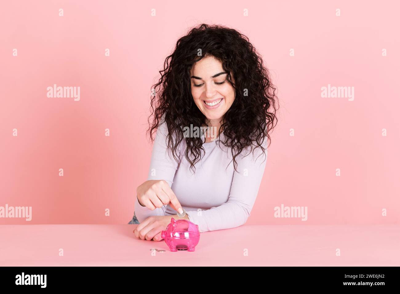 Happy woman saving money in piggy bank against pink background Stock Photo