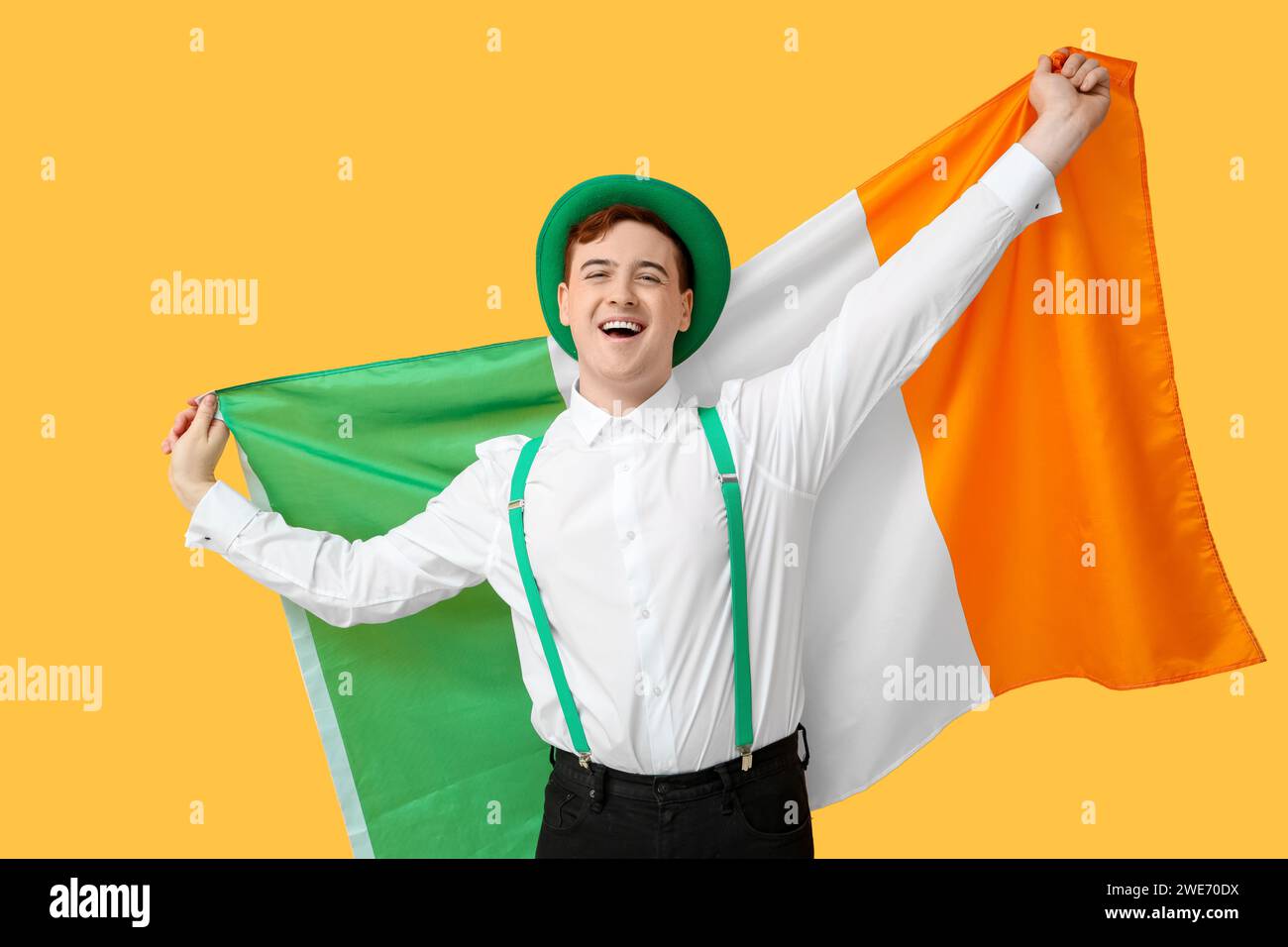 Happy young man in leprechaun's hat with flag of Ireland on yellow background. St. Patrick's Day celebration Stock Photo