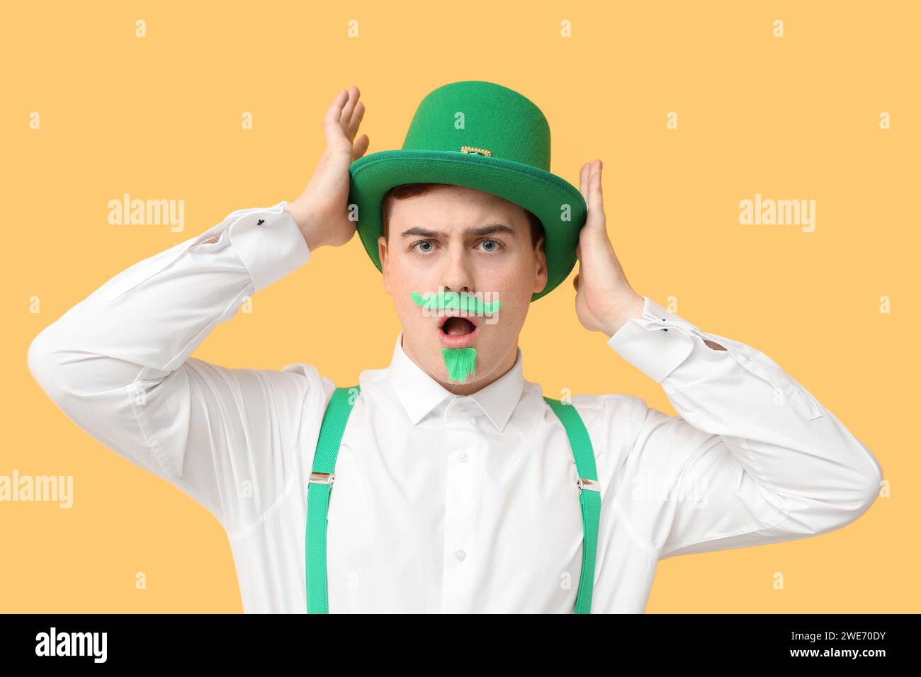 Shocked young man in leprechaun's hat on yellow background. St. Patrick's Day celebration Stock Photo
