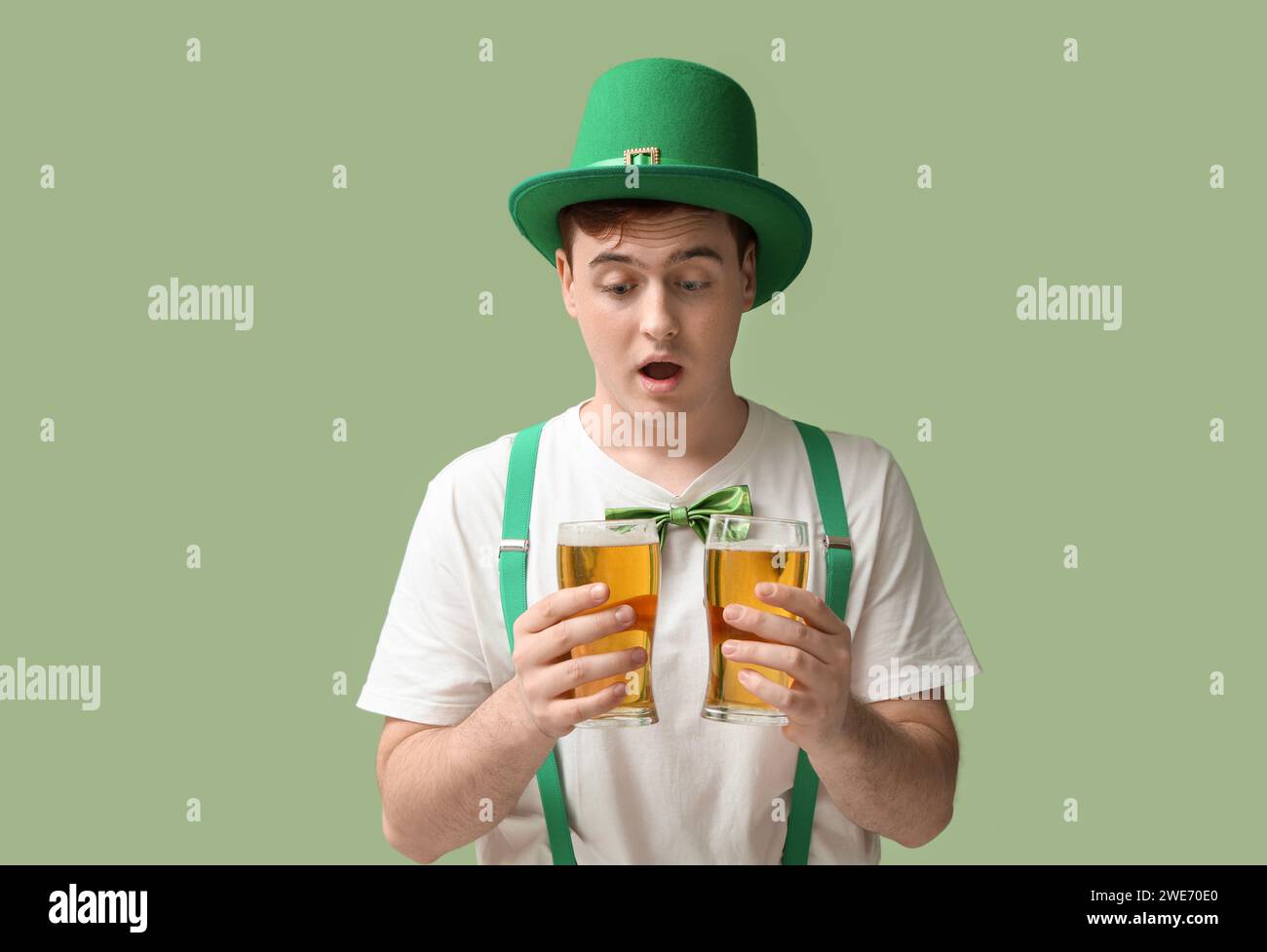 Shocked young man in leprechaun's hat with glasses of beer on green background. St. Patrick's Day celebration Stock Photo