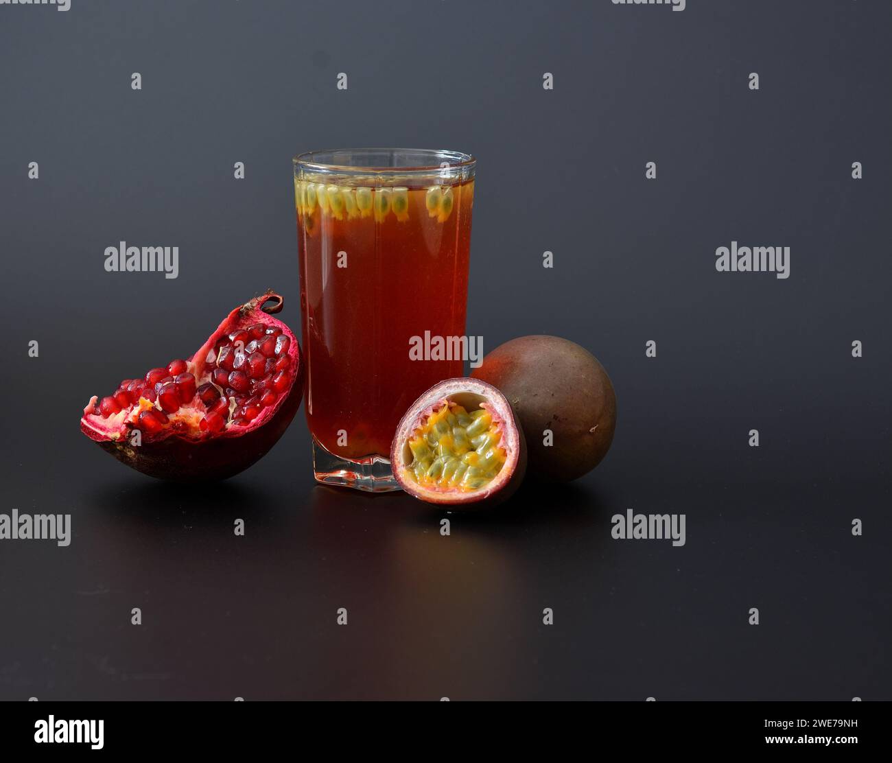 A glass of fruit juice with seeds on a black background, next to a ripe passion fruit and a pomegranate fruit with seeds. Close-up. Stock Photo