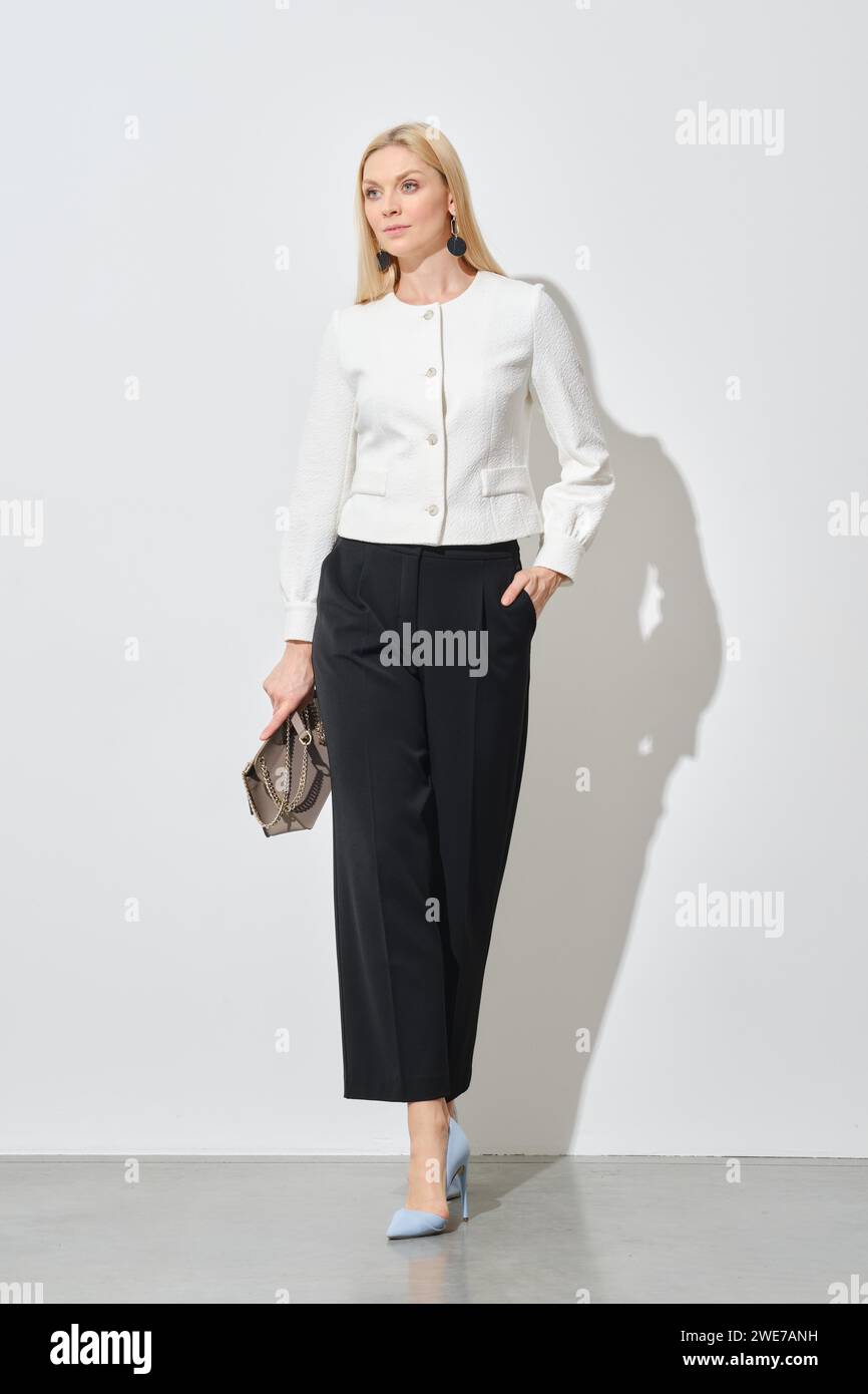 Businesswoman in wide black trousers and short white blazer walking in bright room Stock Photo