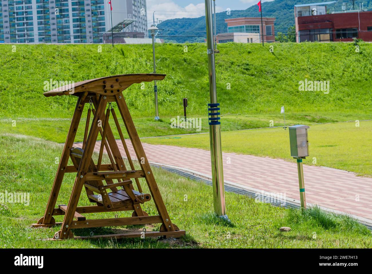 Wooden swing park bench beside walkway with city buildings in