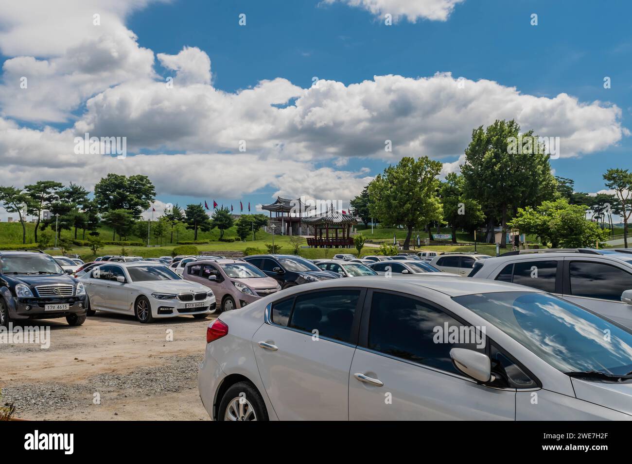 Cars in parking lot with main gate of Hongjueupseong walled town in distance under blue sky in South Korea Stock Photo