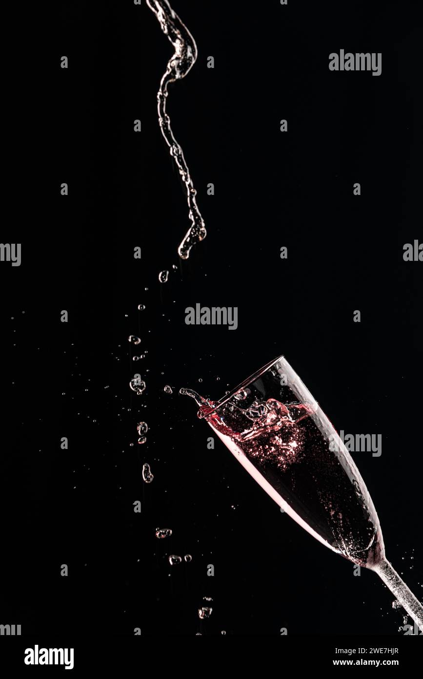 Drops and splashes fly from a champagne glass with rose sparkling wine on a black background Stock Photo