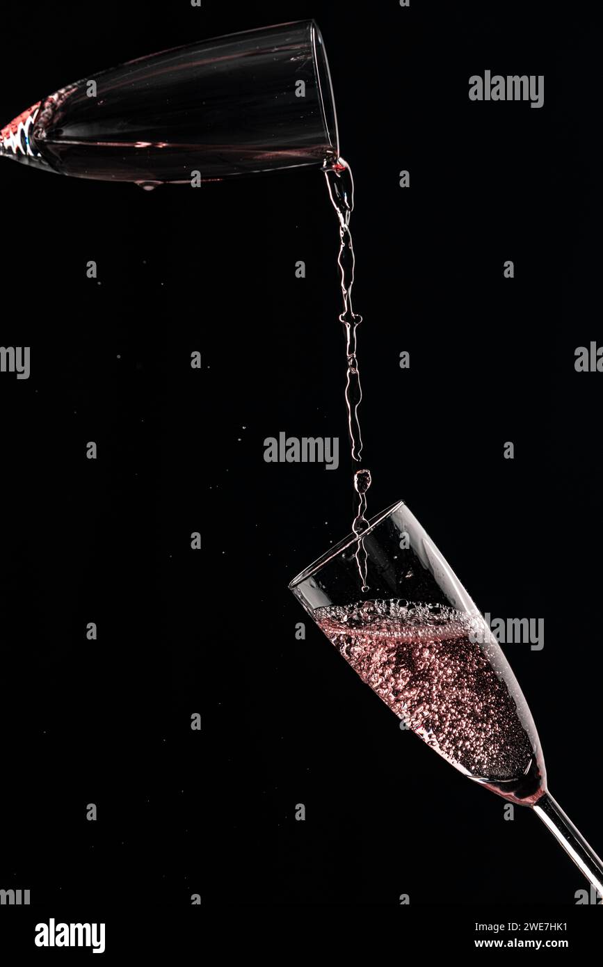 Rose champagne flows from one champagne glass into another, captured in motion, black background Stock Photo