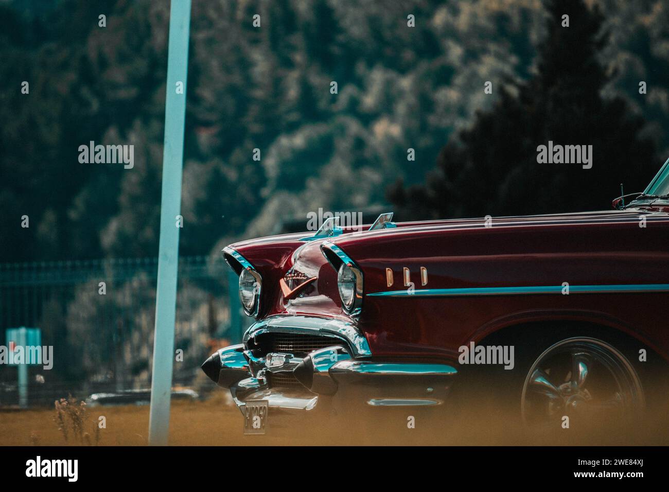 Moody shot of the front of a maroon colored classic car coming around the corner. Stock Photo