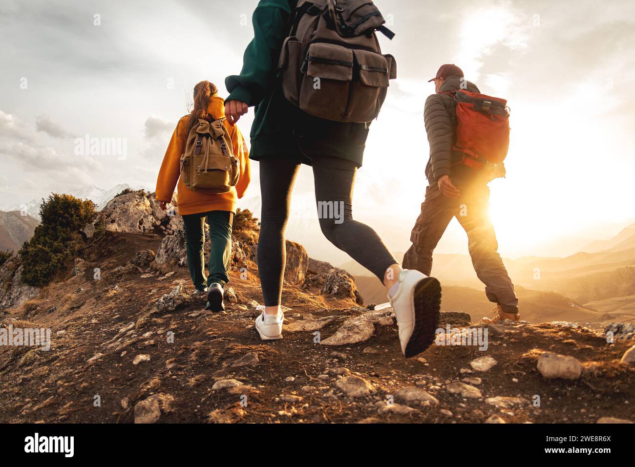 Three young hikers with small backpacks walks in sunset mountains ...