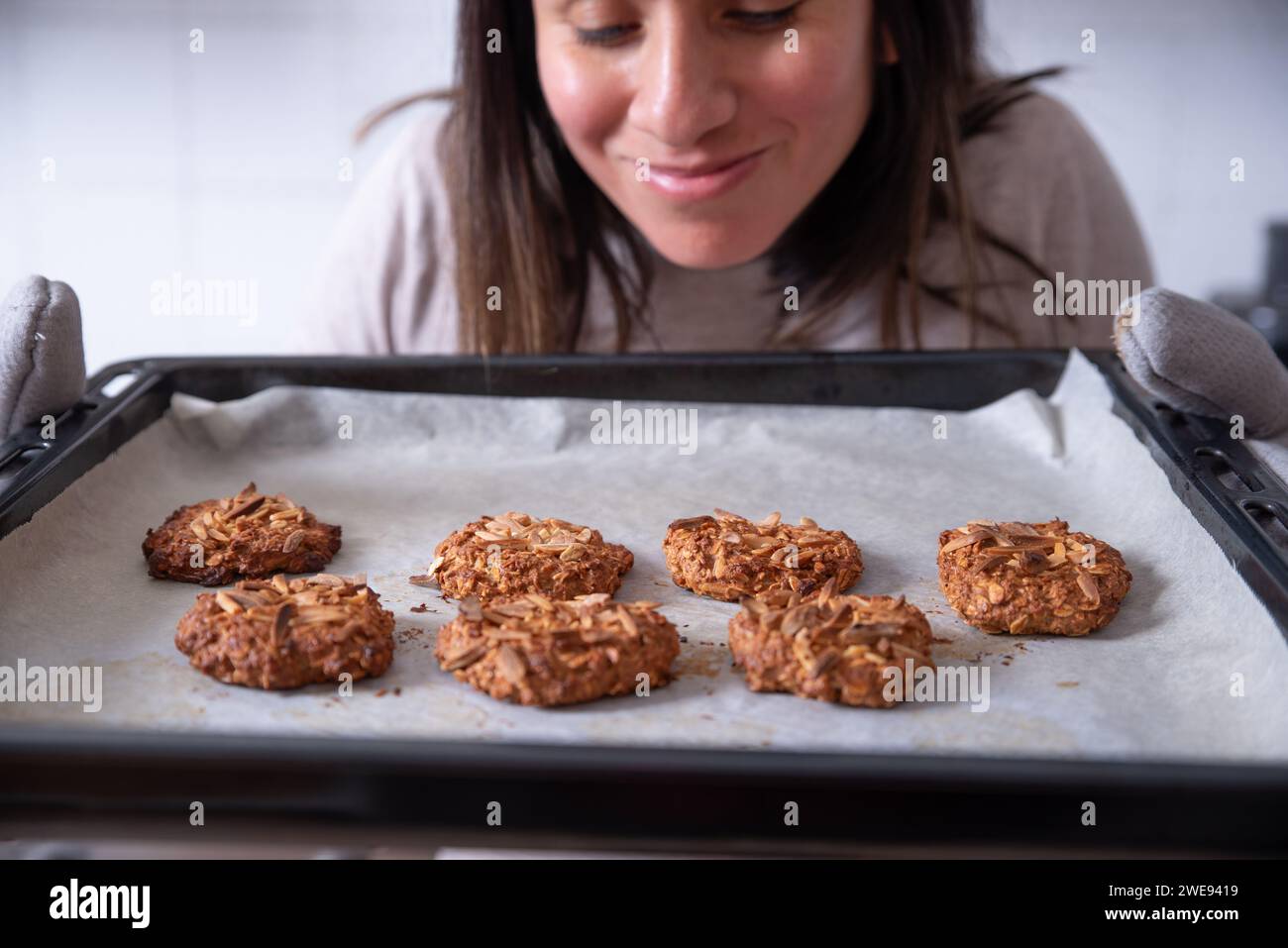 Woman takes freshly baked cookies out of the oven, feeling a pleasant