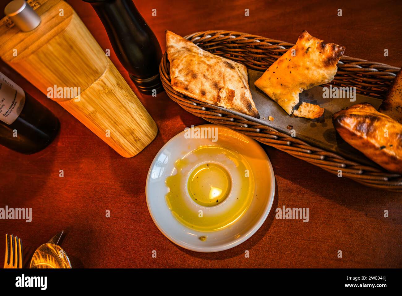 Pastry in wicker basket, olive oil on small plate, spice rack, cutlery on restaurant table. Stock Photo