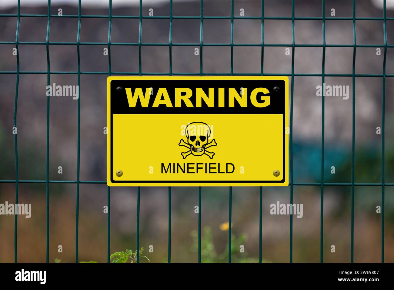 Black and yellow warning sign on a fence displaying a skull and bones symbol and the message in 'Quarantine - Minefield'. Stock Photo