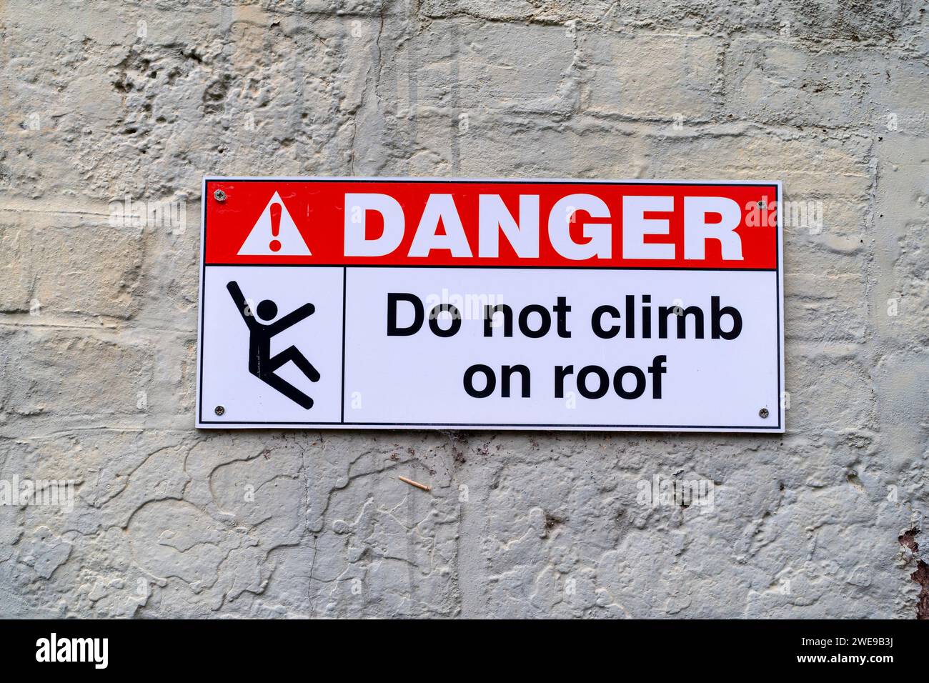 Close up of warning notice in situ on outdoor wall advising public: 'Danger Do Not Climb on Roof' with illustration of falling figure on sign. Stock Photo