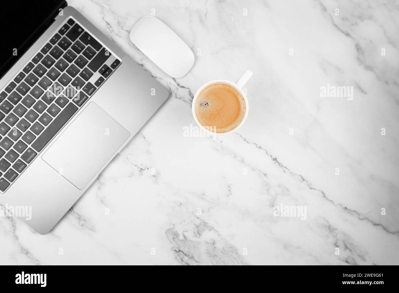 Top view of grey laptop computer on white marble background. Coffee cup, white mouse, flat lay, copy space. Stock Photo