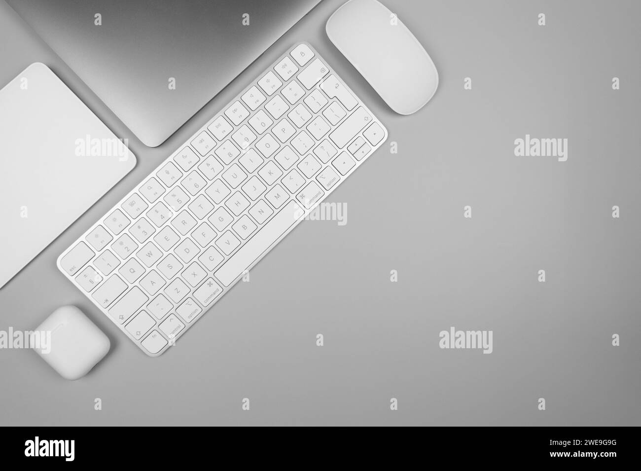 Top view of laptop computer, white keyboard, touchpad, mouse and earphones case on light grey background. Modern office flat lay, copy space. Stock Photo