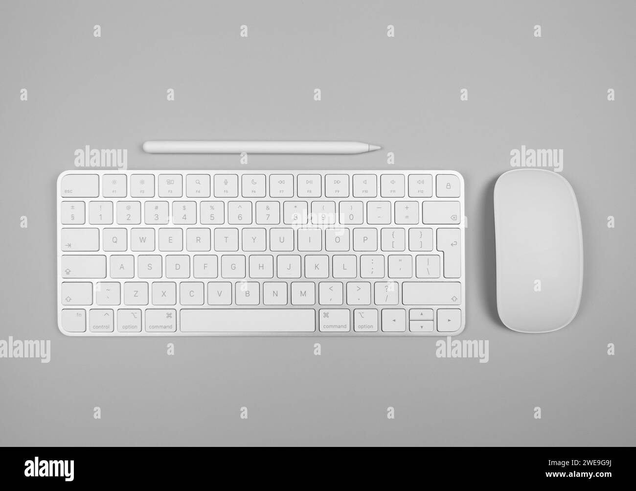 Top view of white keyboard, mouse and pen on light grey background. Modern office flat lay, copy space. Stock Photo