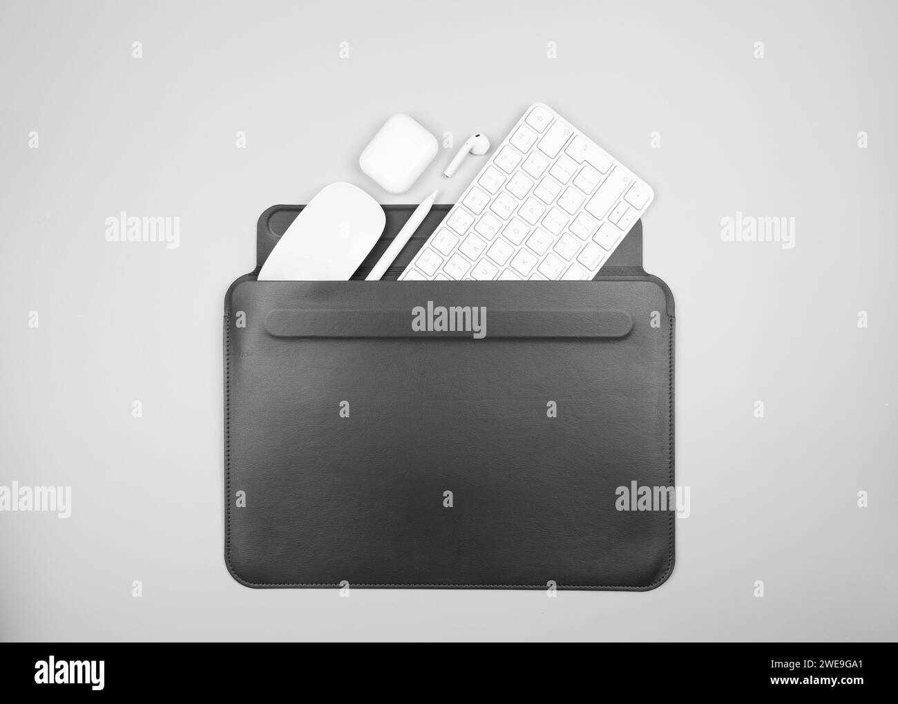 Top view of white keyboard, mouse, earphones case and pen on light grey background. Black laptop computer case flat lay, copy space. Stock Photo