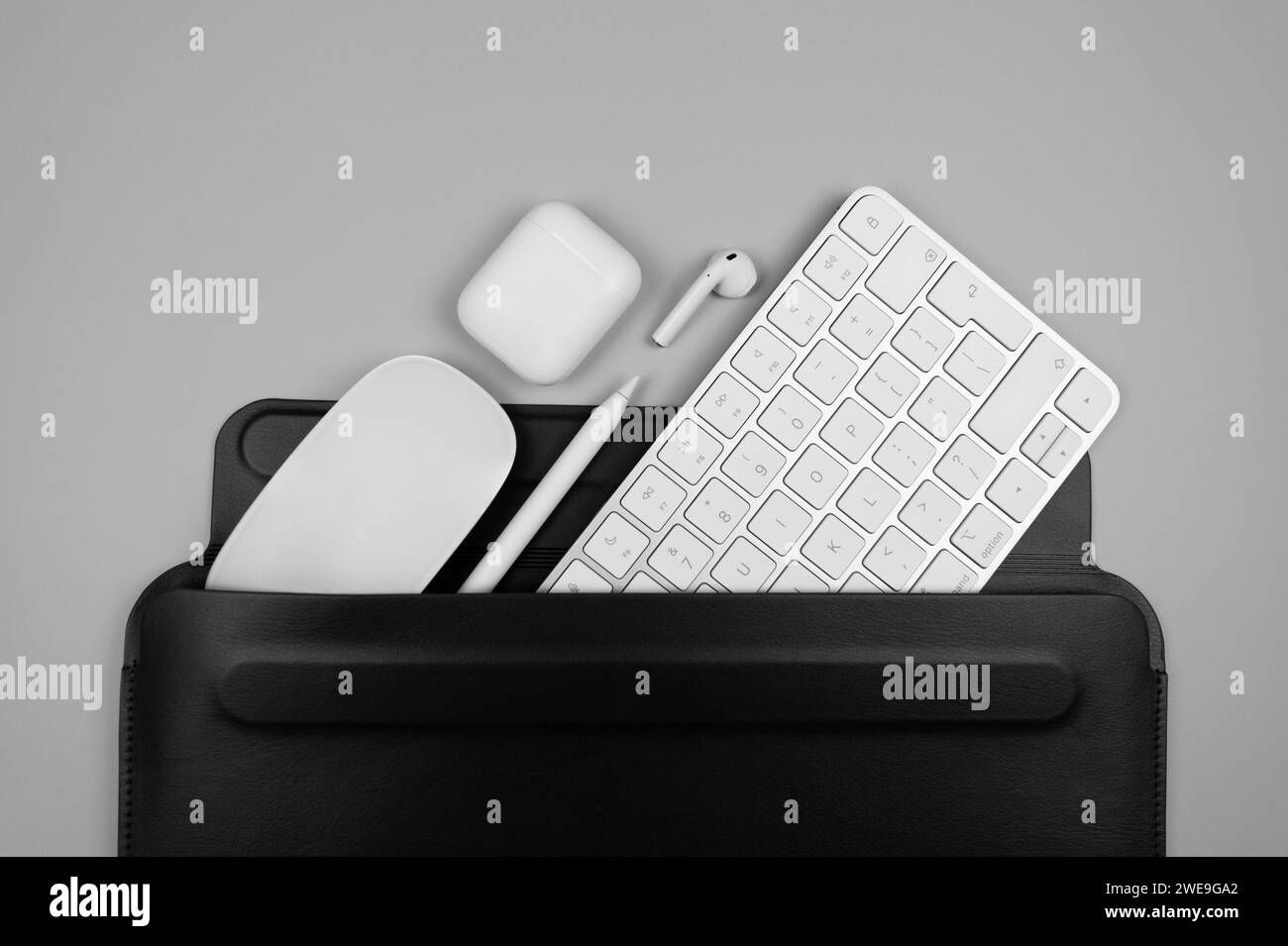 Top view of white keyboard, mouse, earphones case and pen on light grey background. Black laptop computer case flat lay, copy space. Stock Photo