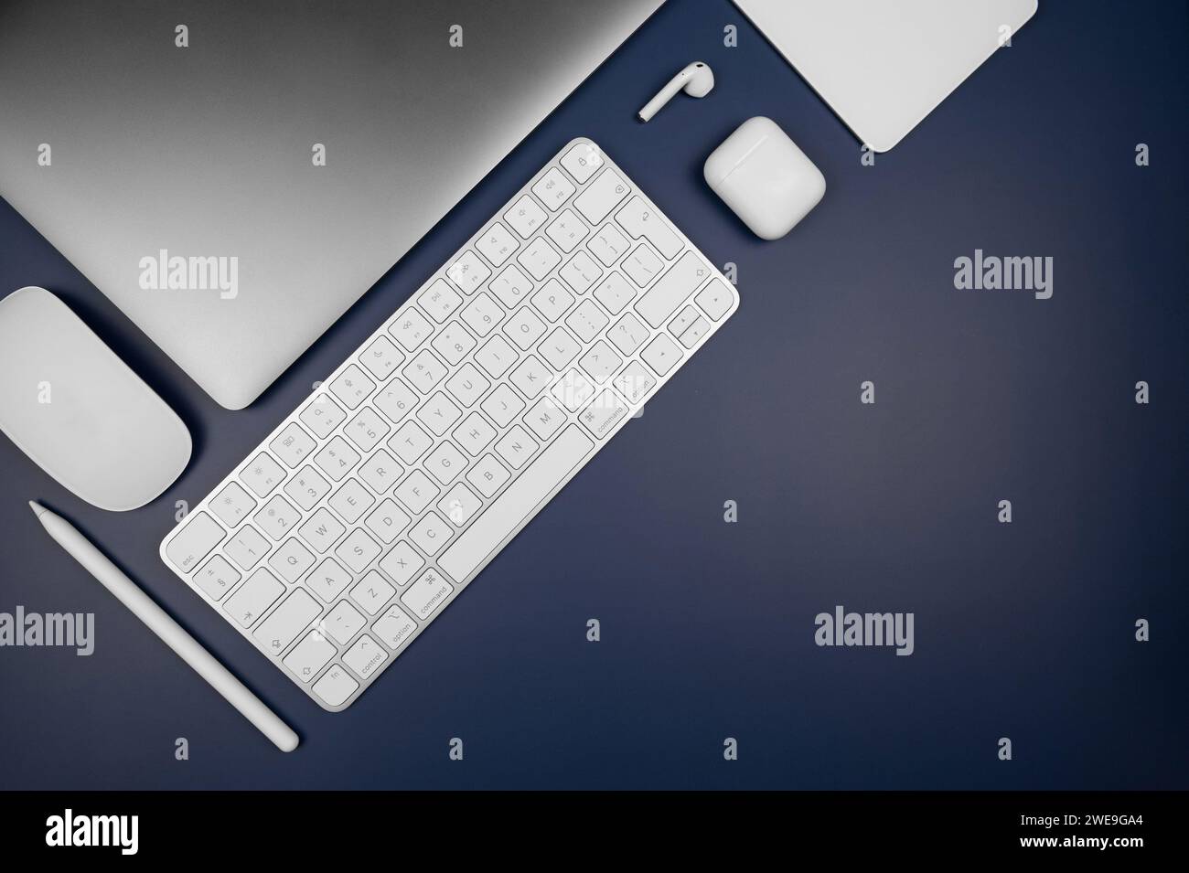 Top view of laptop computer, white keyboard, touchpad, mouse, earphones case and pen on dark blue background. Modern office flat lay, copy space. Stock Photo