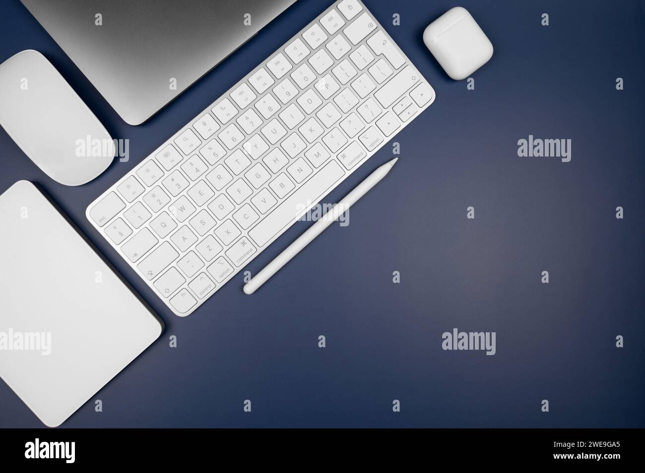Top view of laptop computer, white keyboard, touchpad, mouse, earphones case and pen on dark blue background. Modern office flat lay, copy space. Stock Photo