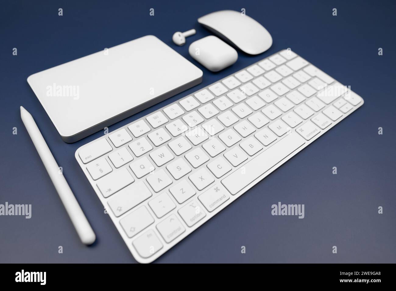White keyboard, touchpad, mouse, earphones case and pen on dark blue background. Modern office, copy space. Stock Photo