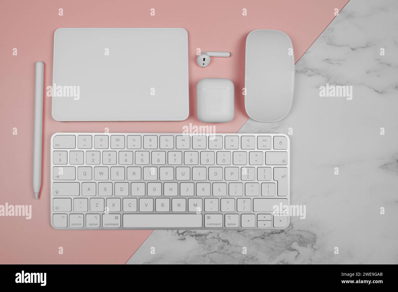Top view of white keyboard, mouse, touchpad, earphones case, pen on pink and white marble background. Modern office flat lay, copy space. Stock Photo