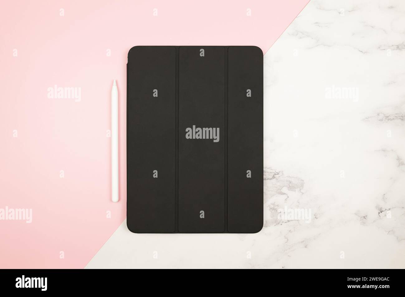 Top view of black tablet case, white pen on pink and white marble background. Modern office flat lay, copy space. Stock Photo