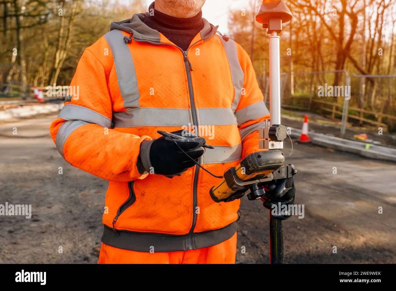 Site engineer operating his touch screen controller instrument during roadworks. Builder using touch screen controller to control total positioning st Stock Photo