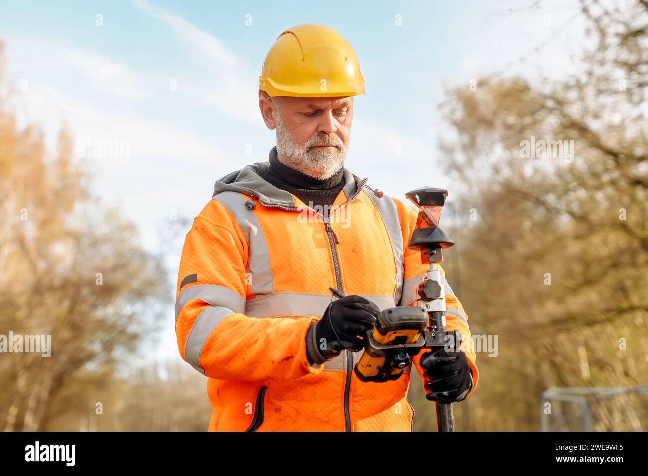 Site engineer operating his touch screen controller instrument during roadworks. Builder using touch screen controller to control total positioning st Stock Photo