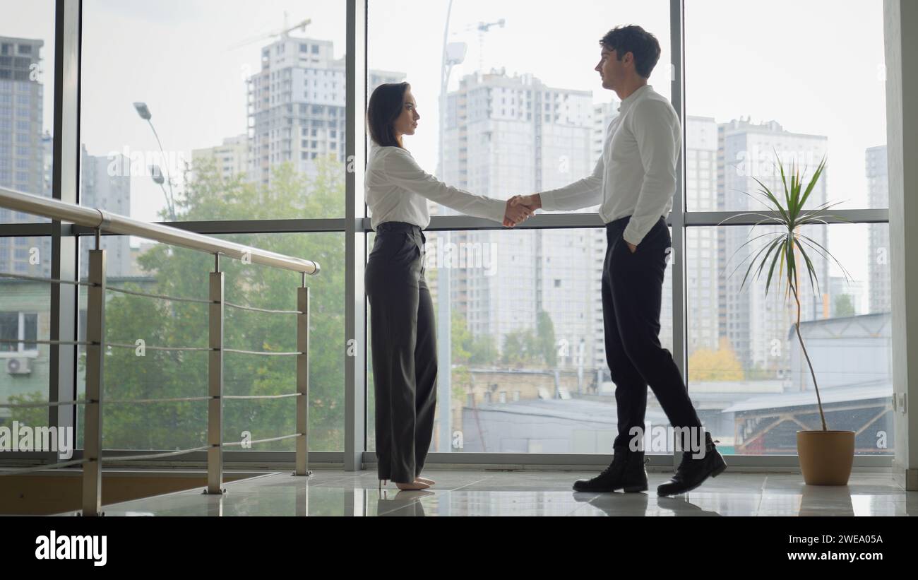 Caucasian businessman and businesswoman shaking hands in office greeting formal meeting colleagues coworkers in company partners handshaking talking Stock Photo