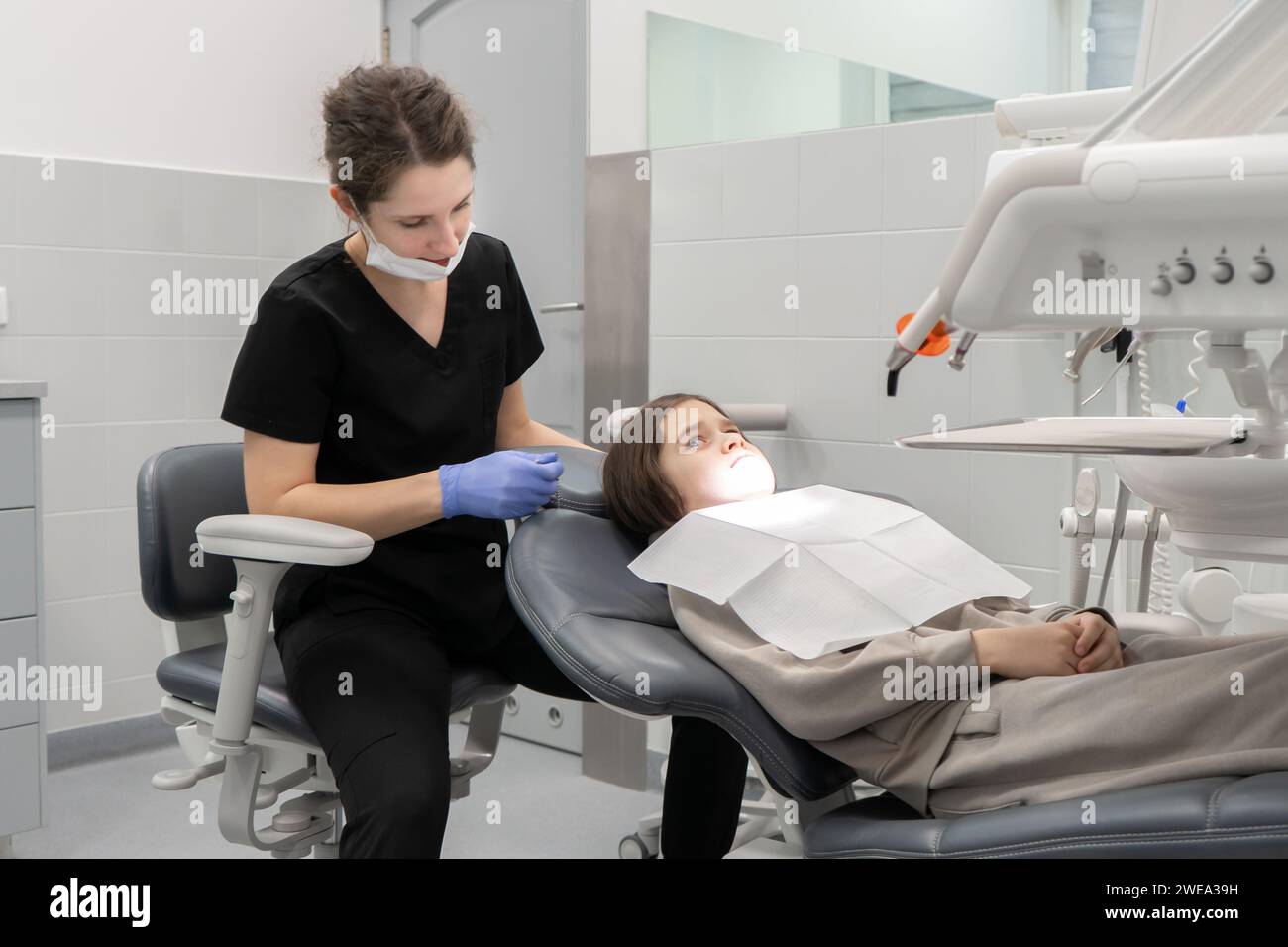 A boy sitting in a dental chair looks at a female doctor in fright. The first preventive medical examination of a child at a pediatric dentist. Stock Photo
