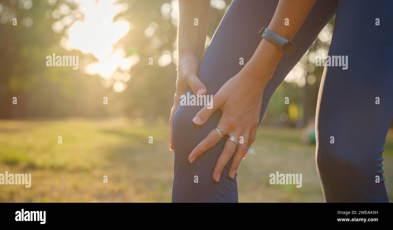 woman with knee pain in evening park. hold her sports injured knee. Low
