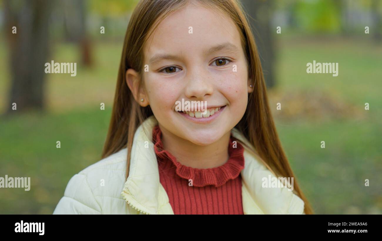 Close up portrait in park autumn alone one beautiful adorable adopted cute teen schoolgirl smiling happy positive Caucasian little girl daughter smile Stock Photo